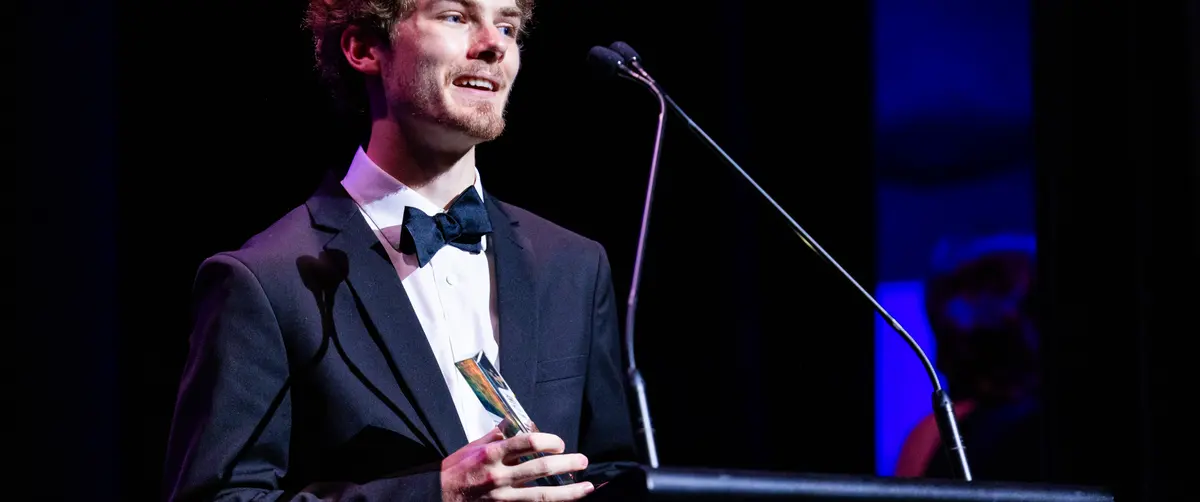 A winner holding his award while speaking at the AFIN 2025 podium.